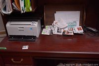 Wide view of dark wood desk with Samsung printer and wood desk tray holding batteries and papers.
