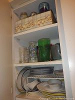 Shelves showing multiple drinking glasses in clear, green, and floral design, several mugs, storage containers, and decorative ceramic pitchers