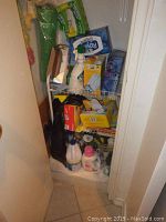 Image showing a white shelving cupboard with several cleaning supplies including bottles of bleach and detergent, tissue boxes, yellow boxes, and spray bottle.