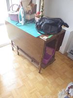 Side view of wooden drop leaf table with one leaf down, showing spindle legs and wooden finish.