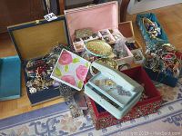 Overview of multiple open jewelry boxes and trays containing assorted costume jewelry items such as bracelets, rings, necklaces, and other accessories.