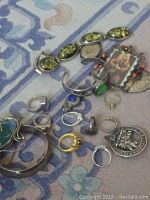 Group view of sterling silver brooches, bracelets, rings, pendant and locket arranged on patterned surface