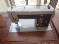 Close-up of Sears Kenmore model 15817560 sewing machine mounted in wooden sewing table with visible dials and needle area