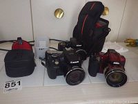 Overview of three digital cameras and two camera bags on white surface