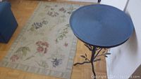 Round metal table with textured glass top and decorative base near wall and parquet floor
