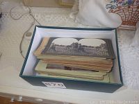 Box filled with vintage stereoscopic viewfinder slides, showing black and white farming images on the top slide