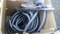 Box containing central vacuum system hose and attachments including extension wand and nozzle.