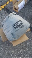 Budge car cover in gray fabric carrying pouch marked with 'BUDGE SINCE 1900 Size-2' placed inside a cardboard box.