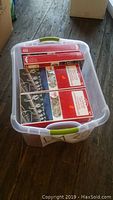 Photo showing clear storage bin filled with multiple boxes of All-Purpose Light Clips, viewed from an angle on the floor.