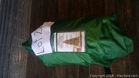 Green storage bag containing the Christmas tree, showing label with product image and instructions on the front.