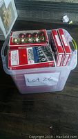 Plastic bin with several unopened boxes of Christmas ornaments and light clips visible from the top showing multiple colors and product packaging