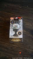 Photo of the snow globe inside its packaging on a wood surface showing front view with design and label.