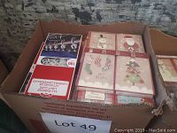 Box with packs of Carlton Christmas cards in various designs including Santa, snowman, Christmas tree, stockings, and phrases like Happy Holidays, Merry Christmas.