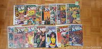Photo showing all 14 X-Men comic books laid out on a wooden floor, displaying colorful covers featuring various X-Men characters and action scenes.