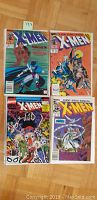 Four X-Men comic books placed on wooden floor showing full front covers of each comic including issue numbers and cover art.