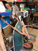 Overall view of the garden tools including wheelbarrow, garden rake with broken tines, and shovels in storage area