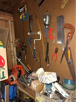 Wide view of pegboard with hand saws, pliers, clamps, paint roller, and other hand tools on a workbench underneath.