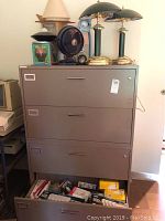Full view of lot on filing cabinet showing lamps, fan, clock, and bottom drawer with lightbulbs.