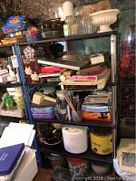 Wide view of shelving with stacked kitchen appliances, boxes, glassware, and miscellaneous kitchen items.