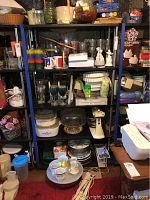 Photo showing shelving unit with various kitchenware including a stand mixer, Corning pie plates, casserole dishes, ceramic figurines, glassware, and other kitchen utensils.
