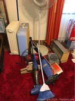 Photo showing fans, vacuums, heaters, and cleaning tools grouped on floor.