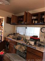 Kitchen countertop and open cabinets showing various dishes, cookware, glassware, and kitchen items including clear glasses, mugs, white bowls, and a stainless steel pitcher.