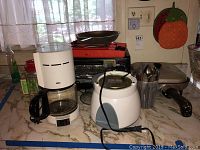Kitchen counter with Braun coffee maker, Toastmaster rice cooker, electric fry pan, Black & Decker toaster oven, and flatware.