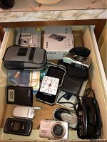 Drawer with multiple digital cameras, film camera, phones, travel clock, and cases
