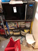 Full view showing Kenmore microwave oven on upper shelf with various plastic storage containers below, alongside other household items.