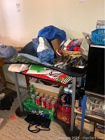 Black metal and glass computer desk with assorted items including a wicker basket with tools, various bags, cans of Sprite and Coca-Cola, and decorative tins.