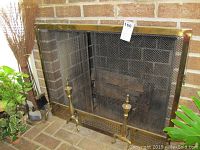 Brass fireplace screen with mesh and brass andirons in front of a brick fireplace, showing overall condition and details of the screen and andirons.