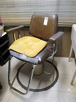 Full view of the hydraulic salon chair showing brown vinyl upholstery, padded armrests, and circular metal base.