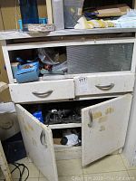Metal cabinet with open drawers and doors, showing hair dryers and miscellaneous items inside.