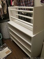 Photo of two white MDF shoe racks positioned near closet with clothes hanging in background, showing multiple shelves and rails on the larger rack.