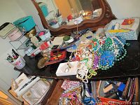 View of dressing table showing multiple costume jewelry items, manicure supplies, and other miscellaneous objects spread out.