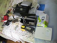 Overview of the lot showing various cameras, carrying cases, a Norelco travel steamer, Philips portable DVD player, cassette tapes and a Sony Ericsson phone.