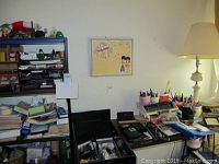 Photo of metal shelves stacked with note pads, papers, binders, black hole punch, calculators, pens in containers, wallet, batteries, and a desk lamp nearby.