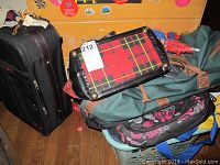Photo showing the black rolling suitcase, green duffle bag, floral backpack, and a plaid tote bag stacked together.