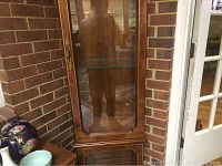 Front view of the vintage wooden and glass curio cabinet showing the door with metal rim and handle, glass shelves inside, and the wood grain finish.