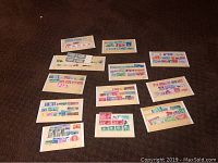 Thirteen small white cards displaying assorted postage stamps of various colors and denominations arranged in rows, photographed from above on brown fabric.