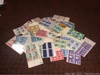 Lot of assorted mint stamps mostly in sets of 4, scattered on a dark surface showing various colors and designs.