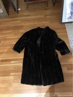 Dark fur coat laid flat on a wooden floor, showing front side with full sleeves and smooth front with no visible damage.