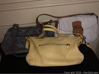 Photo shows three leather purses placed side by side: one dark gray, one beige, one yellow.