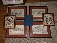 Seven items displayed on carpet: central blue book surrounded by six framed prints and drawings of Williamsburg scenes, including two smaller oval color prints and four larger rectangular black and white sketches.