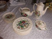 Photo showing coffee pot, sugar bowl, creamer, and stacked dessert plates all with detailed floral designs.