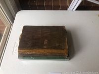 Two hard cover Gone With The Wind books stacked, the top one is the 1936 edition with a worn brown cover, the bottom one is the 1940 edition with a green cover under plastic.