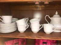 Photo showing the teapot with lid on the right, stacked saucers on the left, and eight stacked tea cups in the middle with embossed floral and scroll details.