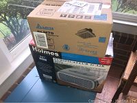 Photo of the stacked boxes showing both the Delta SLM70 ventilation fan box on top and Holmes HEPA air purifier box below by a window.