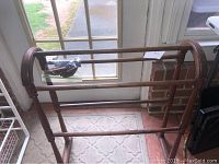 Wooden floor quilt rack in front of a window on a patterned rug, showing the rails and structure of the rack.