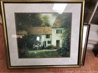 Full view of framed print showing cottage scene with greenery, people, and large white building with thatched roof.